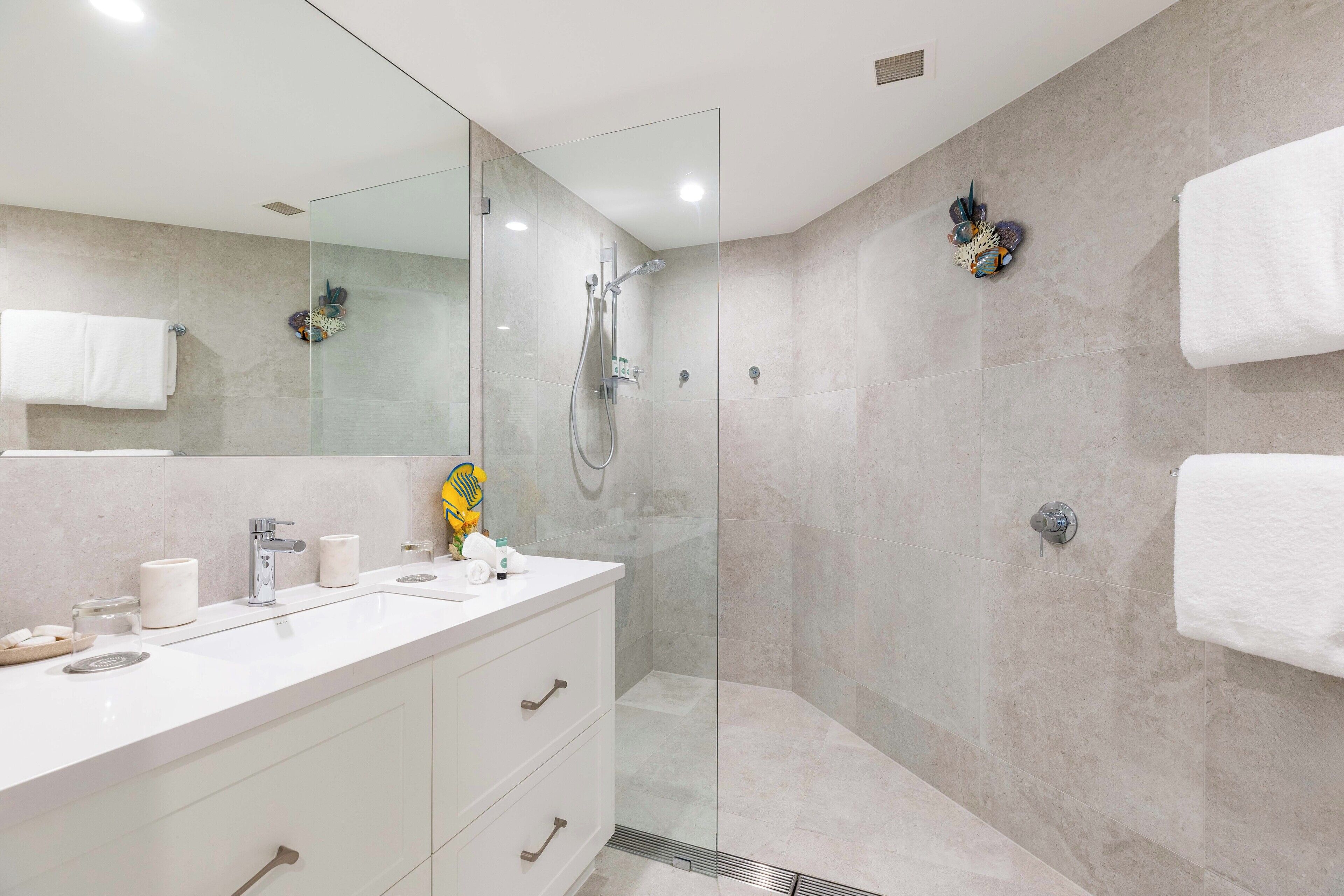 A modern bathroom with a glass-enclosed shower, a white vanity with a mirror, and two white towels hanging on the wall.