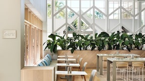 Een modern restaurantinterieur met hoge plafonds, grote ramen en diverse zithoekopstellingen, waaronder tafels en banken.