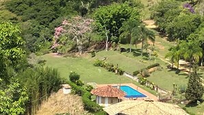 A rural house with a blue swimming pool, surrounded by lush greenery and hills.