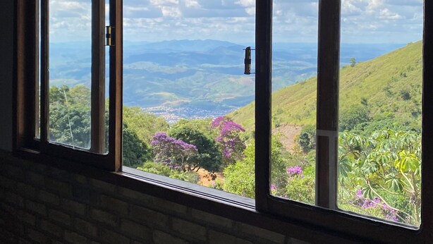 A room with a large window overlooking a mountainous landscape with greenery and purple flowers.