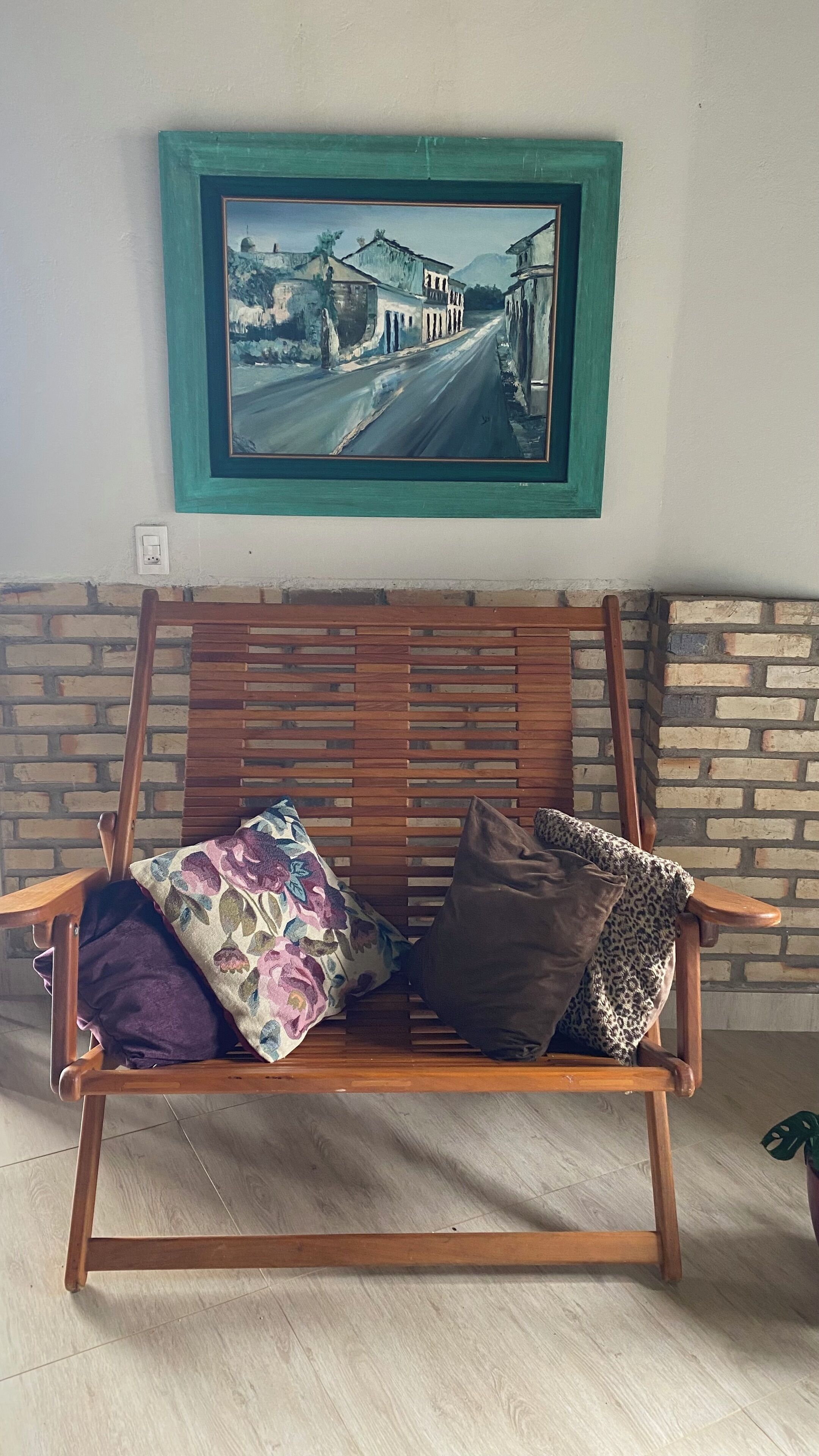 Um banco de madeira com almofadas de padrão floral e de leopardo, em frente a uma parede de tijolos com um quadro emoldurado acima.