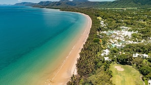 Vista aérea de un complejo turístico en la costa, con playa de arena, abundante vegetación y un campo de golf.