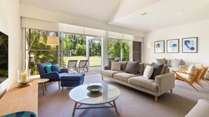 A spacious living room with a large glass coffee table, a sofa, and a dining area with chairs. - Mirage Resort Villa 147 with access to Sheraton Facilities (Port Douglas)