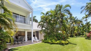 A two-story house with a balcony, a patio with outdoor furniture, and a well-maintained lawn with tropical plants. - Mirage Resort Villa 147 with access to Sheraton Facilities (Port Douglas)