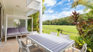 An outdoor patio with a white table and chairs, a white sofa, and a view of a green field. - Mirage Resort Villa 156 with access to Sheraton Facilities (Port Douglas)
