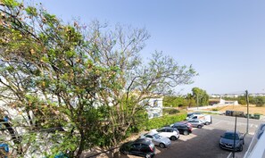 Un parking avec plusieurs voitures, des arbres et un bâtiment en arrière-plan.