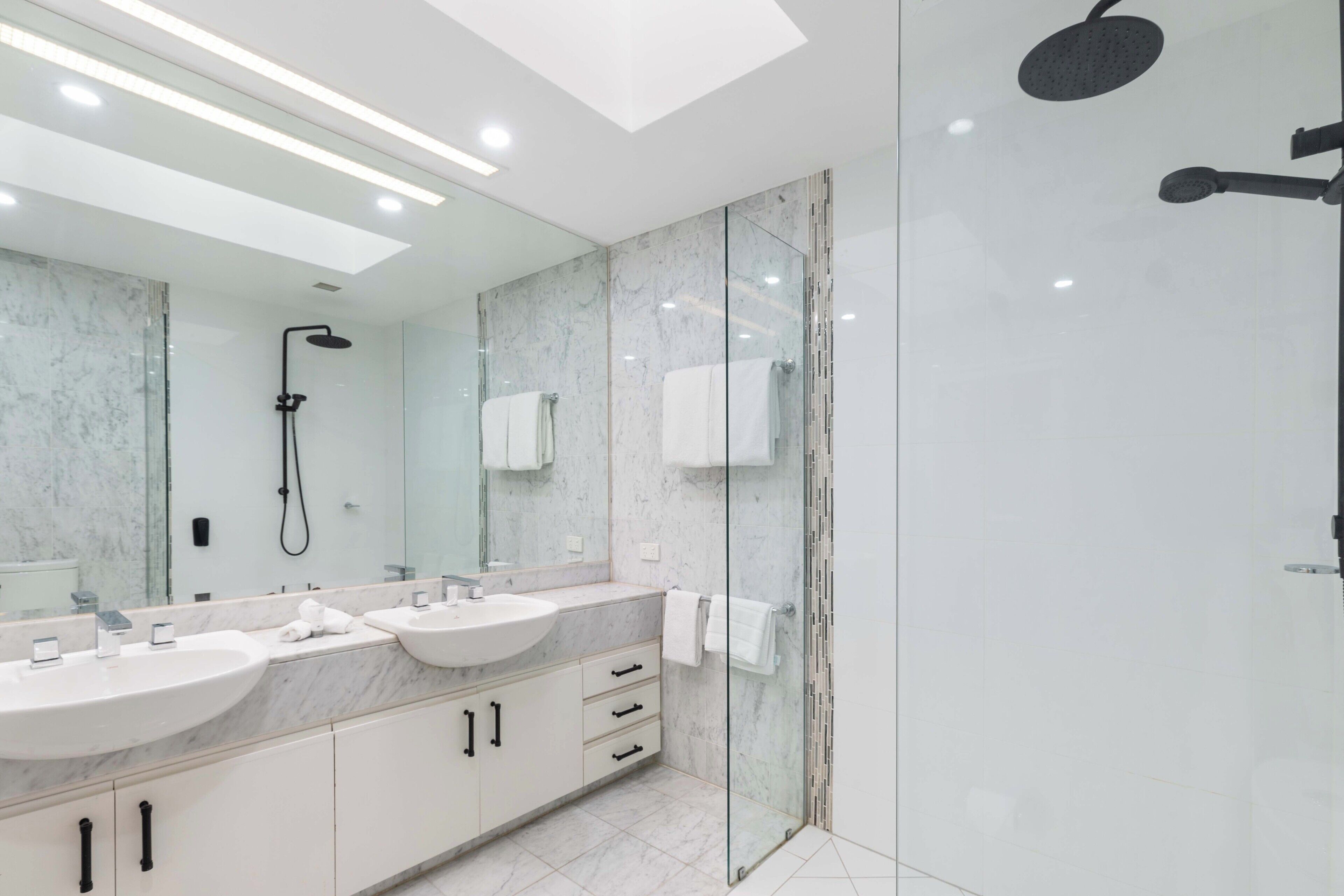 Un baño moderno con dos lavamanos, un espejo grande y zona de ducha con mampara de vidrio.