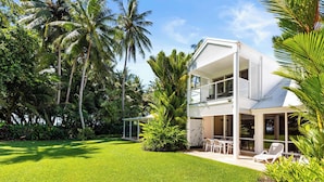 A two-story house with a balcony, surrounded by a well-maintained lawn and palm trees. - Mirage Resort Villa 405 with access to Sheraton Facilities (Port Douglas)