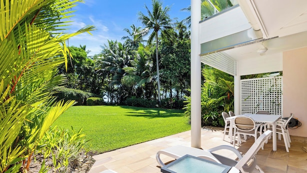 A patio area with a table and chairs, surrounded by lush greenery and a well-maintained lawn. - Mirage Resort Villa 405 with access to Sheraton Facilities (Port Douglas)
