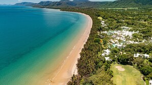 An aerial view of a coastal resort with a sandy beach, dense greenery, and a golf course. - Mirage Resort Villa 405 with access to Sheraton Facilities (Port Douglas)