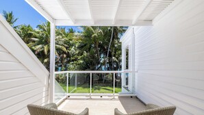 Un balcón techado con sillas de mimbre, baranda de vidrio y vista a un jardín tropical.