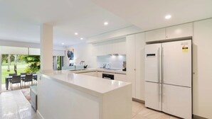 A modern kitchen with white cabinetry, a central island, and a built-in refrigerator. - Mirage Resort Villa 412 with access to Sheraton Facilities (Port Douglas)