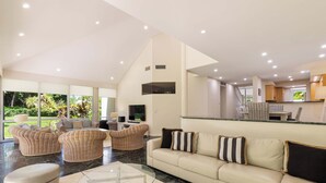 Tilava olohuone, jossa on korkea katto, suuret ikkunat ja keittiö, joka näkyy taustalla.