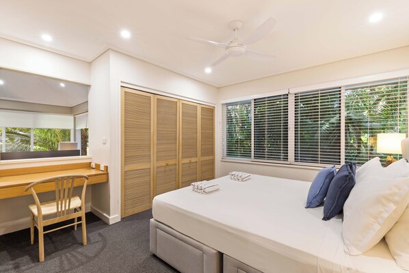 A bedroom with a bed, a desk, a chair, a ceiling fan, and a window with blinds.