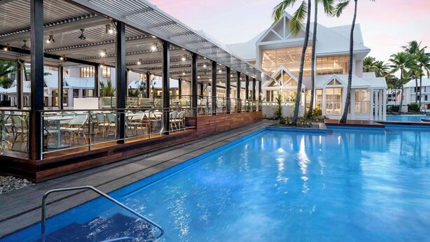 A poolside area with a covered seating area, a pool, and a building with large windows. - Mirage Resort Villa 420 with access to Sheraton Facilities (Port Douglas)