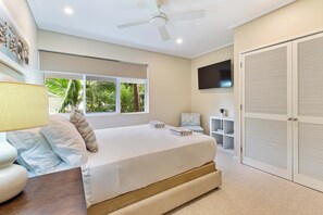A bedroom with a bed, a ceiling fan, a TV, a window, and a wardrobe.