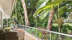 A balcony with wicker furniture, surrounded by lush tropical plants and trees.