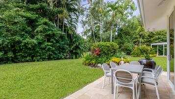 Un patio con una mesa y sillas, rodeado de un césped cuidado y diversas plantas.