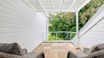 Une terrasse couverte avec deux fauteuils en osier, une balustrade en verre et une vue sur la verdure.