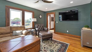 A living room with a sofa, armchair, ottoman, and a television mounted on the wall.