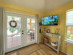 A room with a sliding glass door leading to an outdoor patio, a television mounted on the wall, and a wooden console table with baskets.