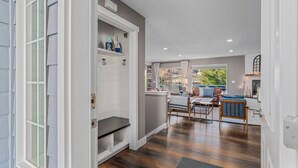 A modern interior with a wooden floor, a bench, a dining area with a table and chairs, and a view of the outdoors.