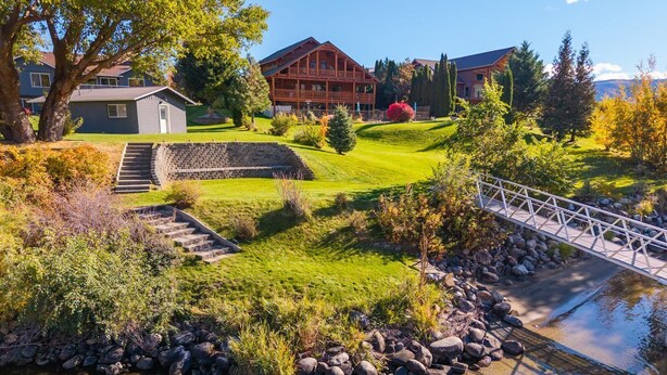 A lodge with a stone staircase leading to a wooden deck, a small pond, and a bridge over the water.