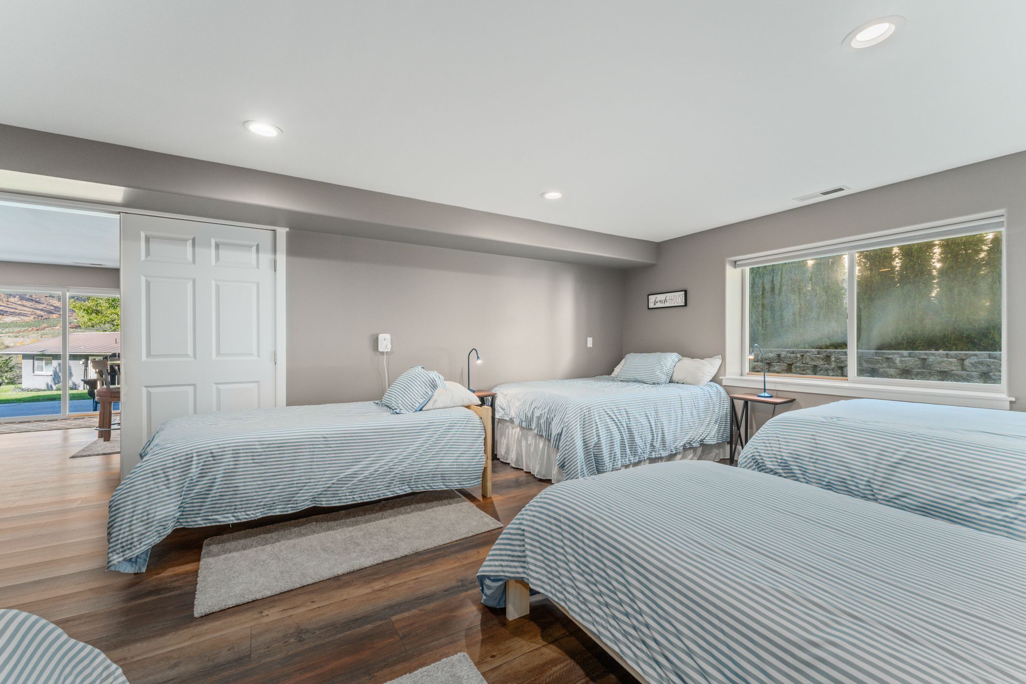 A bedroom with three beds, a large window, and a door leading to a balcony.