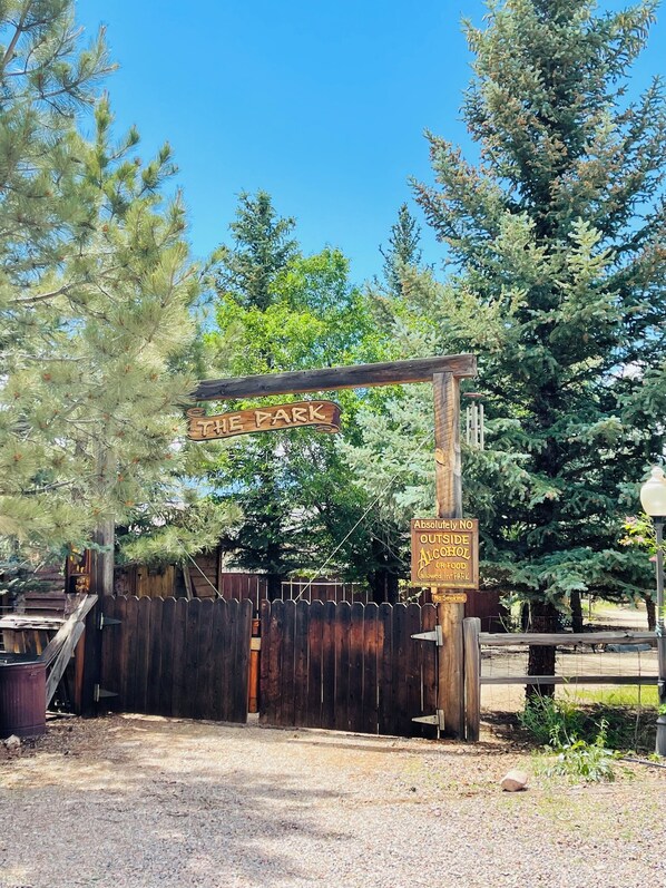 A wooden gate with a sign that reads "THE PARK" and another sign stating "ABSOLUTELY NO OUTSIDE ALCOHOL OR FOOD ALLOWED IN PARK."