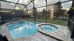 A swimming pool with a hot tub, surrounded by a glass enclosure and a brick deck. - 8909 Disney Retreat – 6BR Home with Pool & Comfort (Kissimmee)