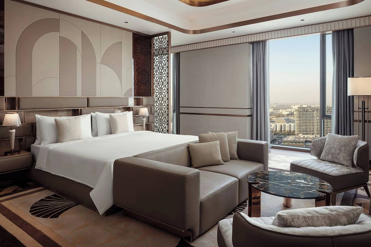 Una habitación de hotel moderna con una cama grande, un sofá, una mesa de centro y vistas a la ciudad.