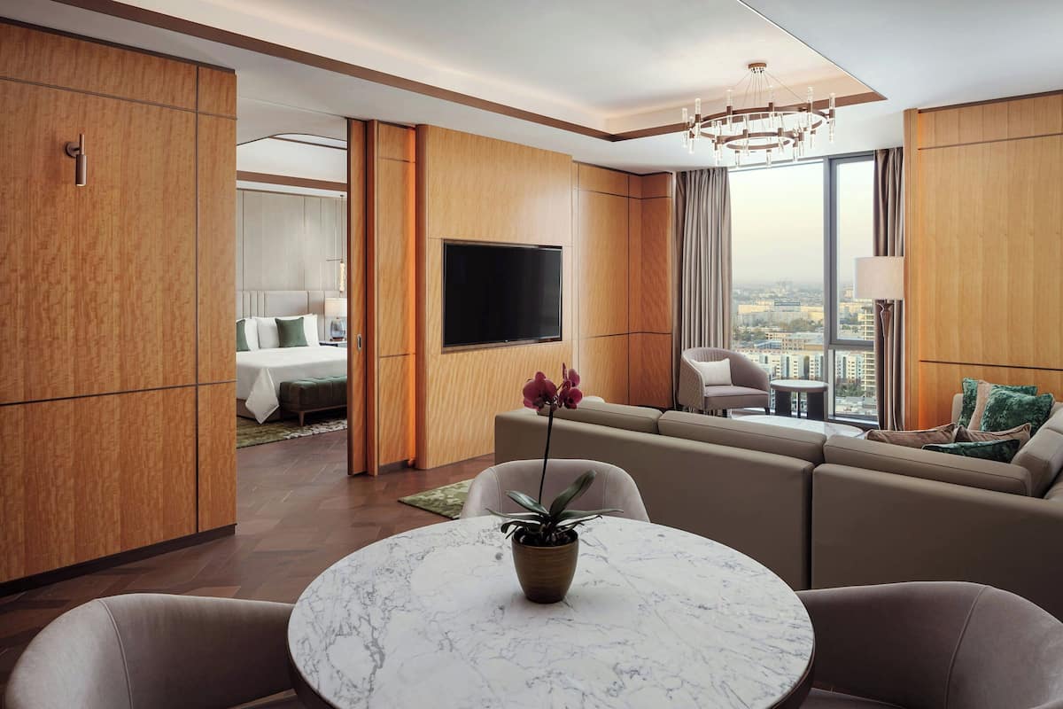 Una habitación de hotel moderna con un televisor grande, asientos cómodos, una zona de comedor y vistas a la ciudad.