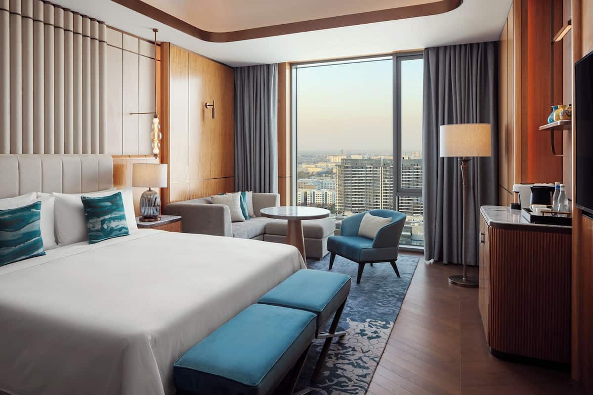 Habitación de hotel con una cama grande, un escritorio, una silla, un sofá y vista a la ciudad por la ventana.