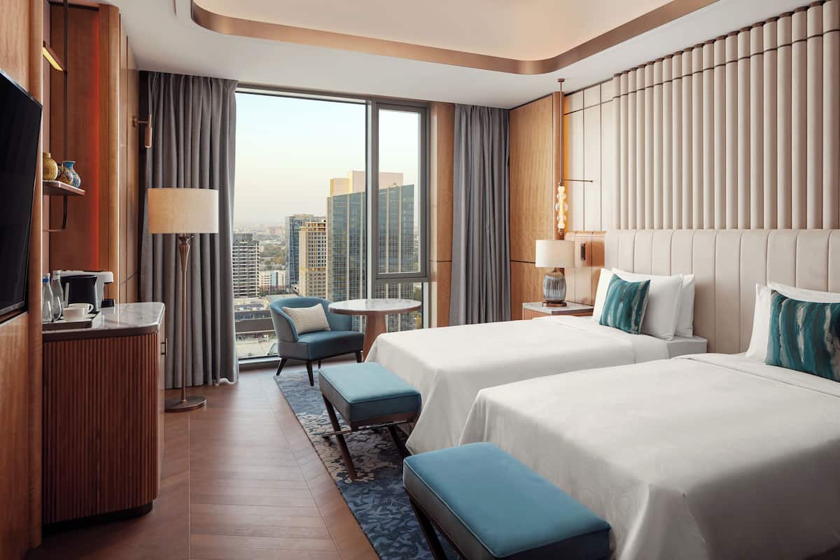 Una habitación de hotel con dos camas, un escritorio, un televisor y vistas a la ciudad.