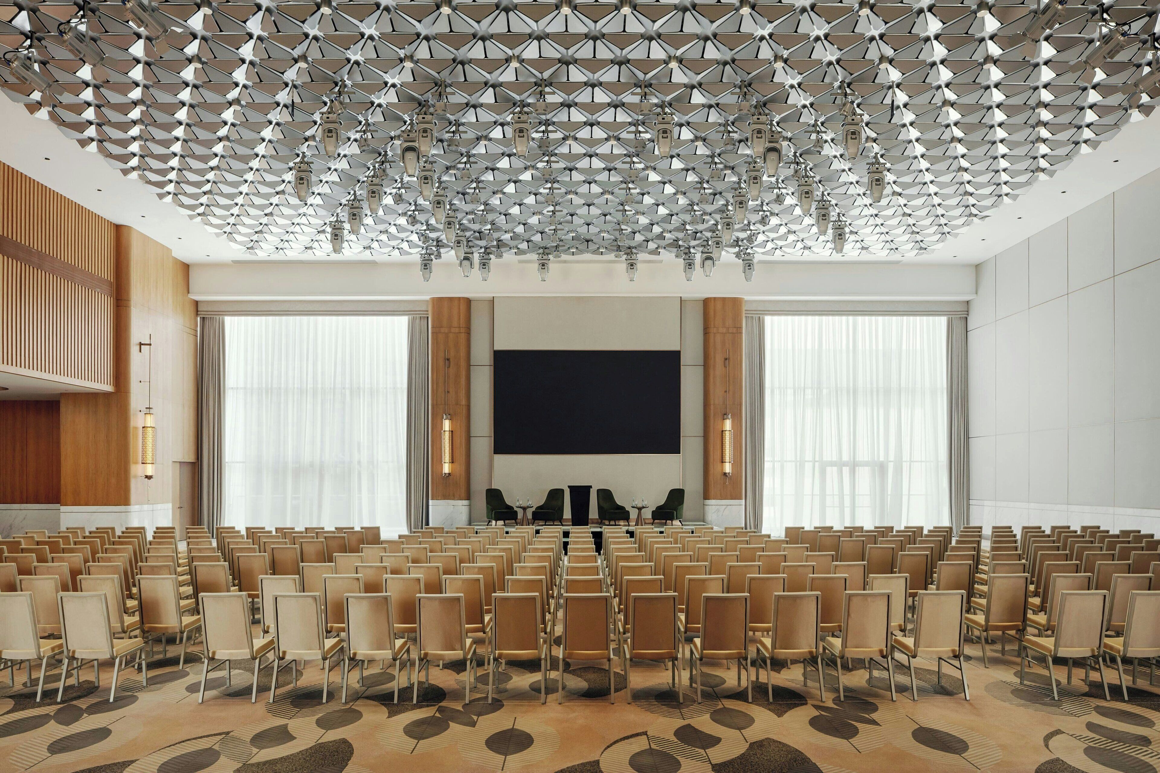 A conference room with rows of chairs, a large screen, and a patterned carpet.