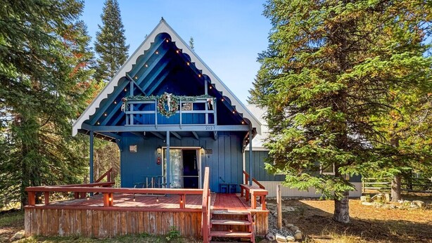 Eine kleine, rustikale Holzhütte mit einer Holzterrasse und einer Veranda, umgeben von Bäumen.