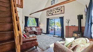 Ein geräumiges Wohnzimmer mit einer Holztreppe, Ledersofas, einem Kamin und einem großen Fenster mit Blick auf eine Terrasse.