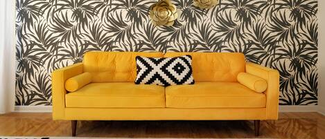 Una habitación con sofá amarillo, papel tapiz estampado y adornos en la pared.