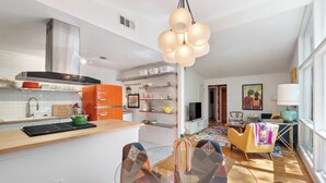A modern kitchen with a central island, a dining area with a glass table, and a living space with a sofa and a large window. - The Big Chill – 4BR 2.5BA, Sleeps 10, Auburn Retreat Near Downtown & Campus (Auburn)