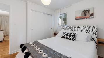 Ein ordentlich eingerichtetes Schlafzimmer mit einem großen Bett, einem gemusterten Kopfteil und einem Fenster mit Vorhängen.