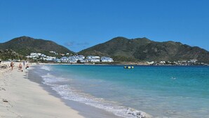 A beach with clear blue water, sandy shore, and distant hills. - Luxury Sea-View 2 Bedrooms,  Duplex town house, Pool, private OrientBeach Access (Orient bay)