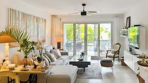 A modern living room with a sofa, coffee table, and dining area. There is a television on the wall and a ceiling fan. - Luxury Sea-View 2 Bedrooms,  Duplex town house, Pool, private OrientBeach Access (Orient bay)