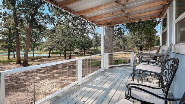 A covered porch with a wooden ceiling, white railing, and a bench. - Pixie's Porch Tiny Home (Centerville)