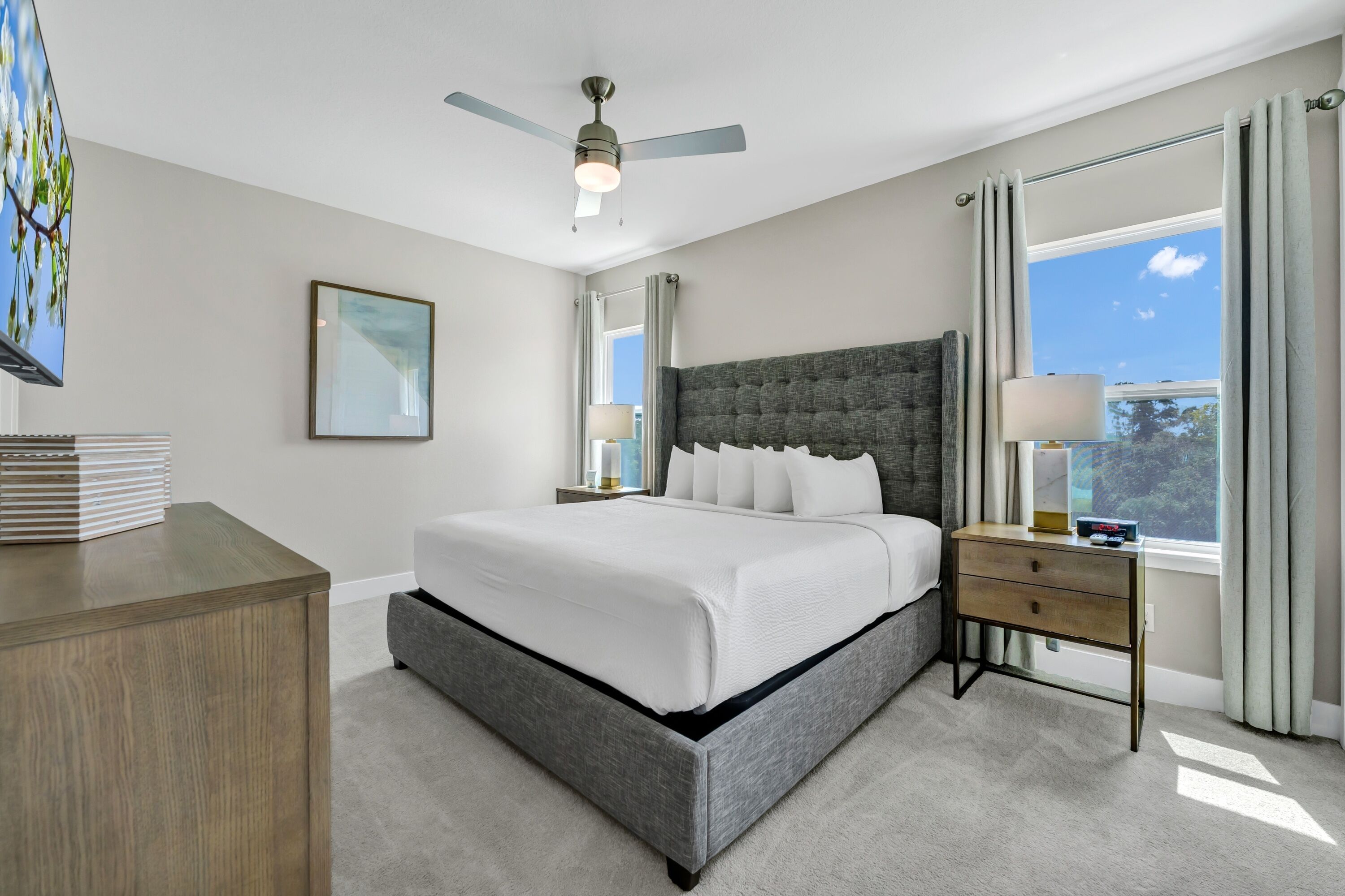 A modern bedroom with a large bed, a ceiling fan, a nightstand, and a window with curtains.