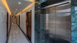 Un pasillo moderno con pared de mármol, un ascensor y una puerta de madera.