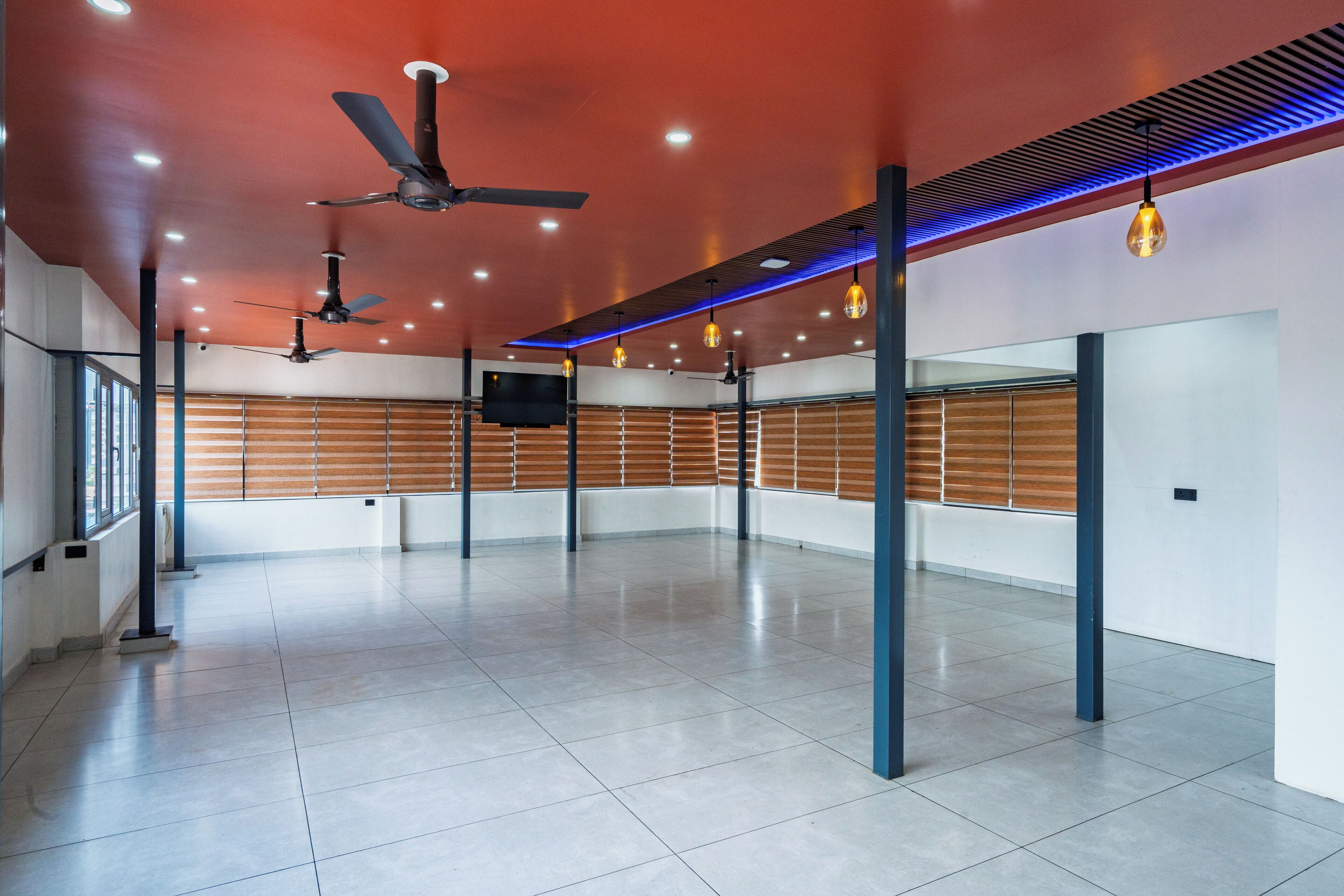 A spacious, modern room with a red ceiling, multiple ceiling fans, recessed lighting, and a large flat-screen TV mounted on the wall.