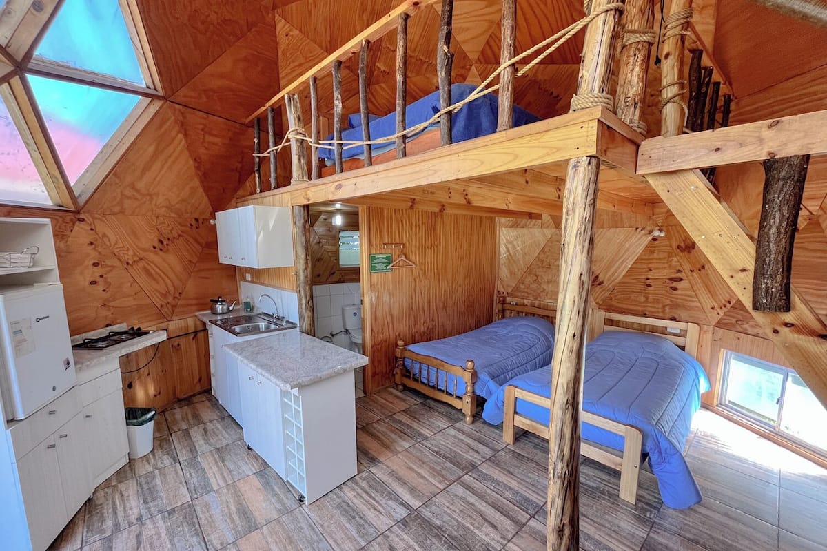A compact wooden cabin with a loft bedroom, a kitchenette, and a bathroom.
