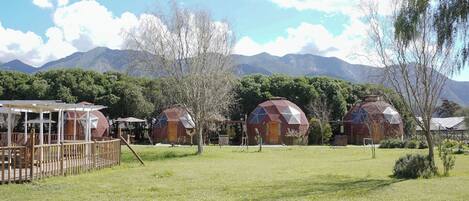 A rural setting with three geodesic dome structures, a wooden deck, and a mountain backdrop.