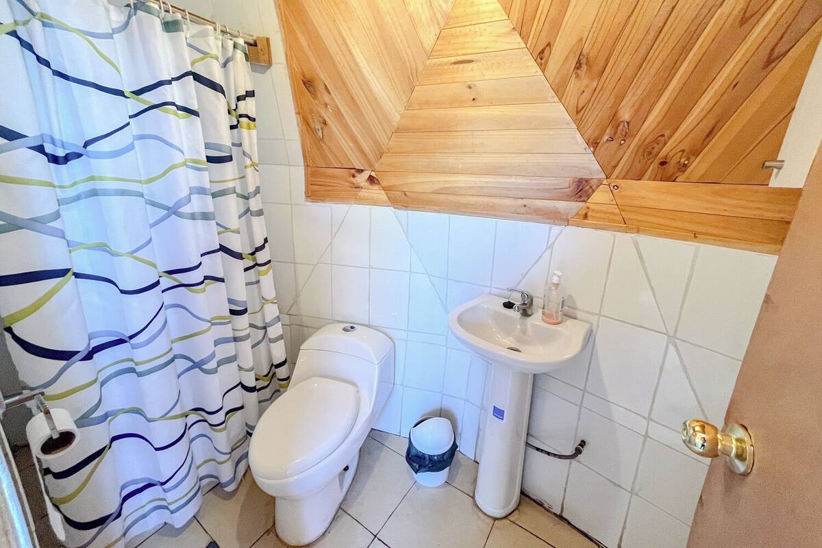 A bathroom with a striped shower curtain, a toilet, a sink, and wooden paneling on the ceiling.
