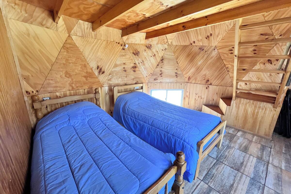 A wooden cabin room with two beds, a small window, and a sloped ceiling.